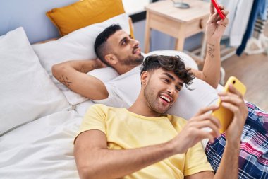 İki erkek yatak odasında akıllı telefon kullanıyor.