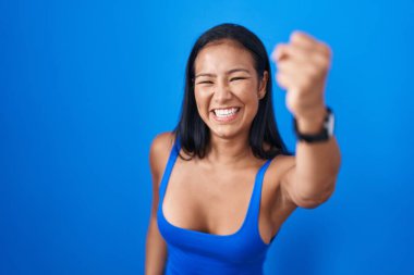 Mavi arka planda öfkeli ve kızgın duran İspanyol kadın öfkeyle bağırırken yumruğunu kaldırıyor ve öfkeleniyor. öfke ve agresif konsept. 