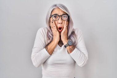 Beyaz arka planda beyaz saçları olan orta yaşlı bir kadın. Korkmuş ve şok olmuş. Şaşırmış ve şaşırmış bir halde. 