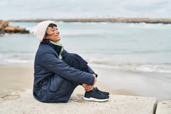 Młoda Piękna Latynoska Uśmiecha Się Pewnie Siedząc Podłodze Nad Morzem — Zdjęcie stockowe