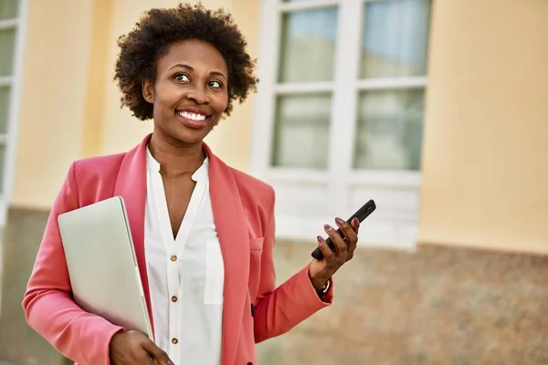 Beautiful business african american woman with afro hair smiling happy and confident outdoors at the city using smarpthone