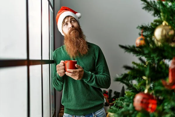 Молодой Рыжий Мужчина Пьет Кофе Стоя Рождественской Елки Дома — стоковое фото