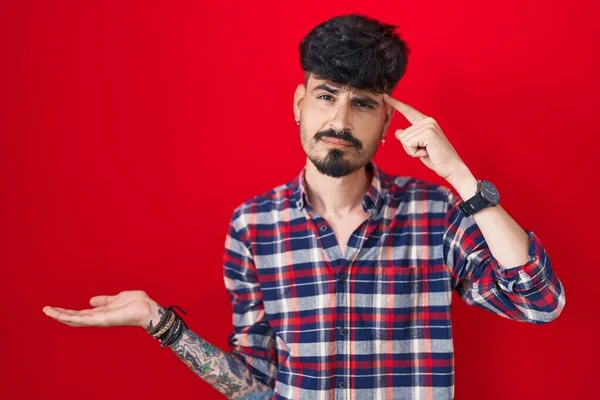Joven Hombre Hispano Con Barba Pie Sobre Fondo Rojo Confundido —  Fotos de Stock
