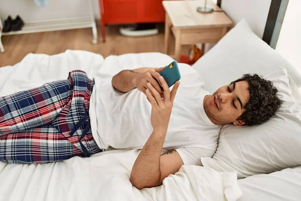 Young Hispanic Man Using Smartphone Lying Bed Bedroom — Zdjęcie stockowe