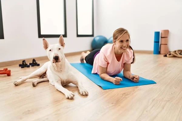 Young caucasian woman smiling confident training abs exercise with dog at sport center