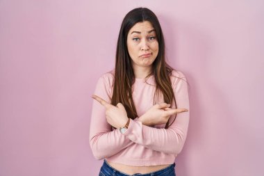 Pembe arka planda duran genç esmer kadın her iki tarafı da parmaklarıyla işaret ediyor, farklı yönler farklı. 