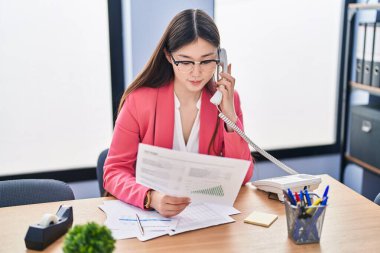 Çinli iş kadını telefonda konuşuyor. Ofiste belgeleri okuyor.