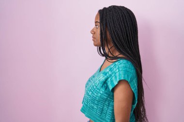 Pembe arka planda dikilen örgülü genç Afro-Amerikalı. Yan tarafa bakıyor, rahat bir görünüm takınıyor ve kendine güvenen bir gülüşü var.. 