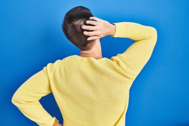 Hispanik adam mavi arka planda dikiliyor. Elleri kafasında şüpheyi düşünüyor. 