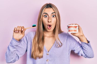 Takma diş ve diş fırçası tutan güzel İspanyol kadın şaşkınlık ve şaşkınlık dolu bir ifade, korku ve heyecanlı bir yüz ifadesiyle dehşete düşmüş ve şok olmuştu.. 
