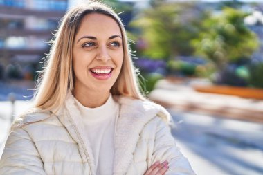 Kendine güvenen genç bir kadın caddede kollarını kavuşturmuş duruyor.