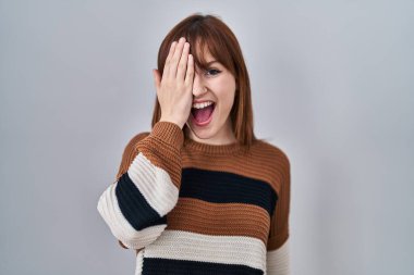 İzole edilmiş arka planda çizgili süveter giyen genç güzel bir kadın bir gözünü eliyle kapatıyor, yüzünde kendine güvenen bir gülümseme ve sürpriz bir duygu var.. 