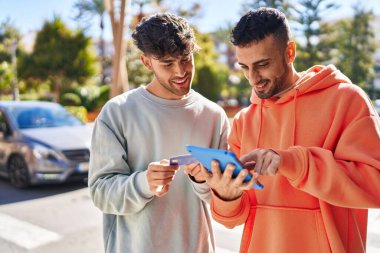 Caddede dokunmatik ped ve kredi kartı kullanan iki erkek.