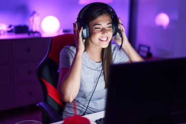 Young beautiful hispanic woman streamer playing video game using computer at gaming room