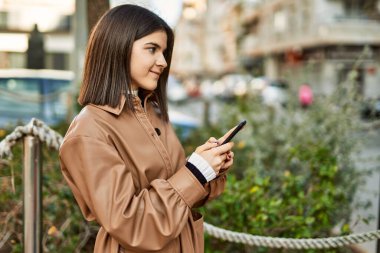 Genç, güzel esmer kadın dışarıda mutlu bir şekilde gülümsüyor akıllı telefon kullanıyor.