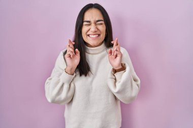 Pembe arka planda duran genç Güney Asyalı kadın umut ve gözleriyle gülümseyerek işaret ediyor. Şans ve batıl inançlar. 