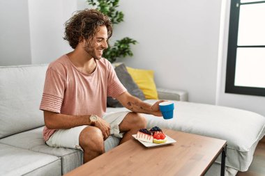 Genç İspanyol adam kahvaltısını yapıyor. Evdeki kanepede oturuyor..
