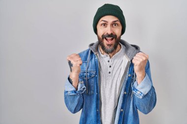 Young hispanic man with tattoos wearing wool cap celebrating surprised and amazed for success with arms raised and open eyes. winner concept. 