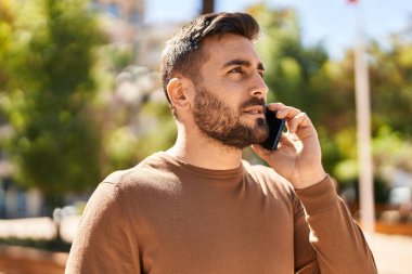 Genç İspanyol adam parkta akıllı telefondan konuşuyor.