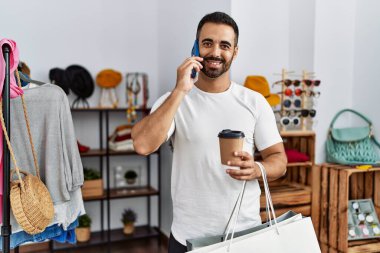 Young hispanic man customer talking on the smartphone shopping at clothing store