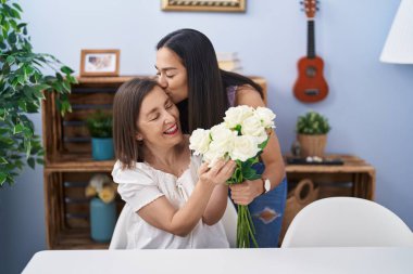 Two women mother and daughter surprise with bouquet of flowers at home