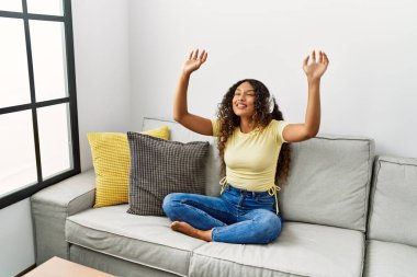 Evde müzik dinleyen, kendinden emin, gülümseyen genç Latin kadın.