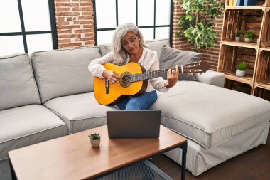 Orta yaşlı bir kadının evde online gitar dersi var.