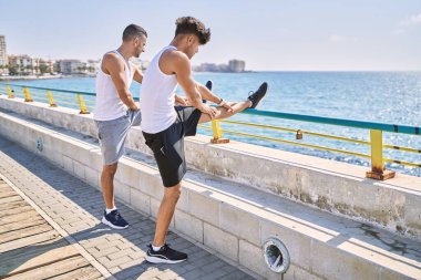 Two hispanic men couple stretching at seaside
