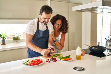 Orta yaşlı İspanyol çift gülümsüyor. Kendilerine güveniyorlar ve mutfakta yemek pişiriyorlar.