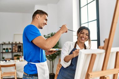 Resim okulunda boya fırçasıyla oynarken gülümseyen iki öğrenci..