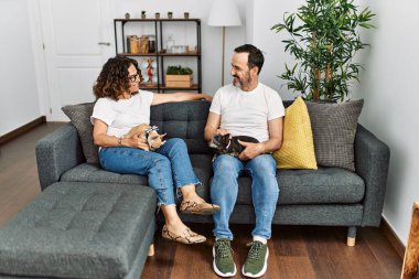 Orta yaşlı, gülümseyen bir çift evde köpeklerle birlikte kanepede oturuyor..