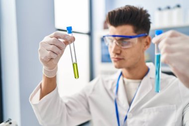 Laboratuvarda test tüpleri tutan bilim adamı üniforması giyen İspanyol bir genç.
