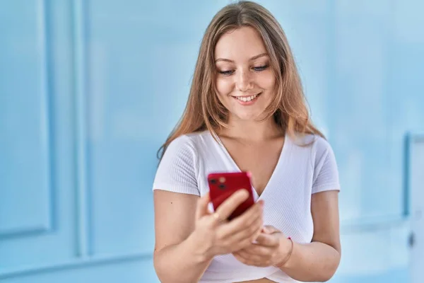 Junge Blonde Frau Lächelt Selbstbewusst Mit Smartphone Über Isolierten Blauen — Stockfoto