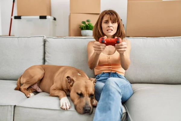 Young caucasian woman playing video game sitting on sofa with dog at home