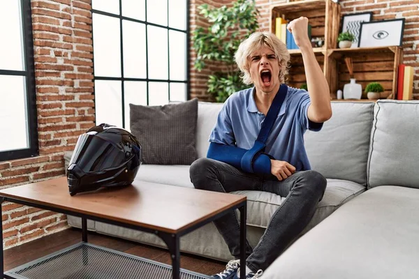 Young man wearing arm on sling for motorcycle accident annoyed and frustrated shouting with anger, yelling crazy with anger and hand raised