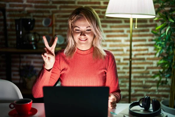 ブロンド女性使用ノートパソコンで夜にホームショーとポイントアップとともに指番号2ながら笑顔自信と幸せ — ストック写真