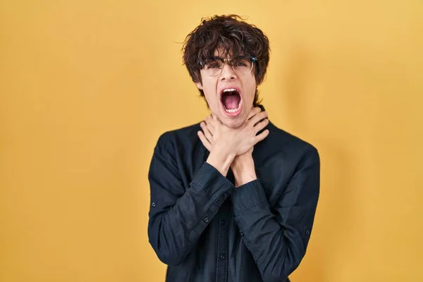 Joven Con Gafas Sobre Fondo Amarillo Gritando Sofocándose Por Estrangulamiento —  Fotos de Stock