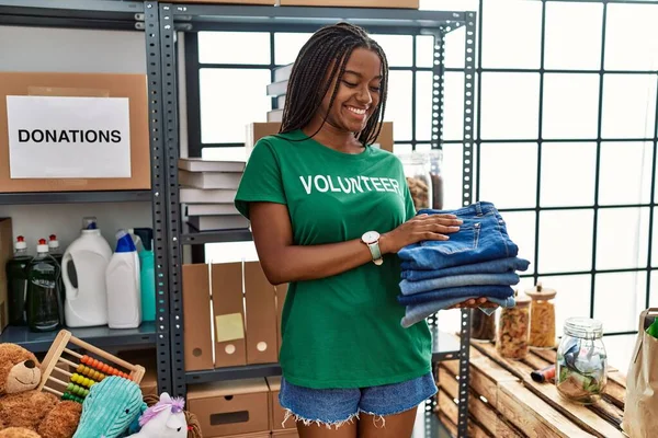 Young African American Woman Wearing Volunteer Uniform Holding Folded Jeans — Stock fotografie