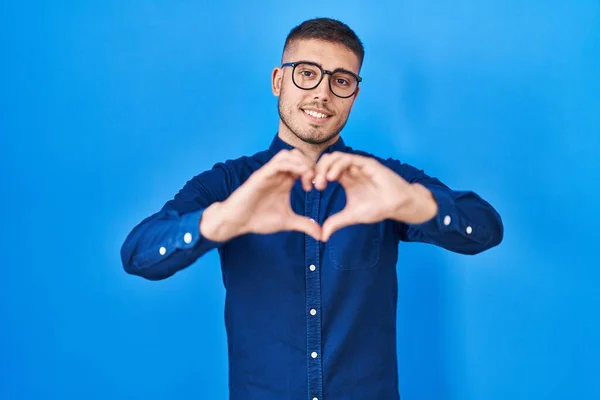 Mladý Hispánec Nosí Brýle Nad Modrým Pozadím Usmívá Lásce Rukou — Stock fotografie