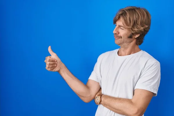 Middelbare Leeftijd Man Staan Blauwe Achtergrond Kijken Trots Glimlachen Doen — Stockfoto