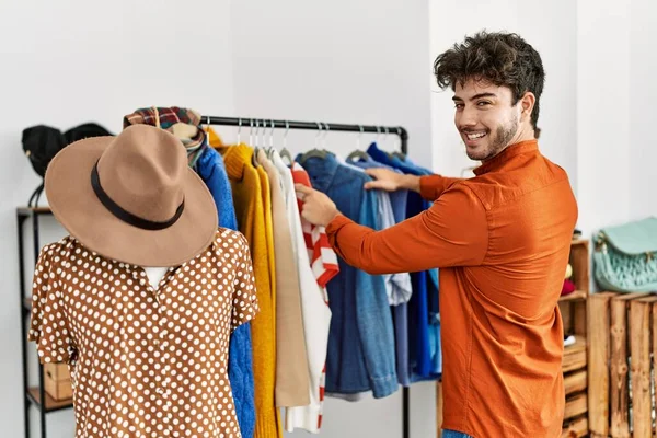 Young hispanic customer man smiling happy choosing clothes at clothing store.