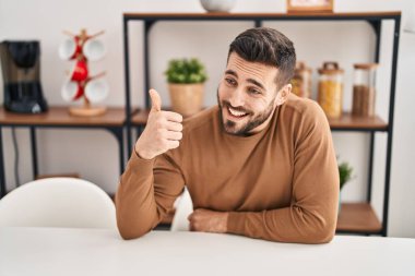 Latin kökenli genç adam işaret diliyle evde masada oturuyor.