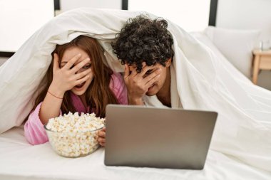 Genç çift yatak odasındaki yatakta film seyrediyor..