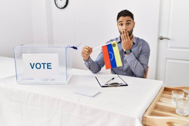 Siyasi seçim kampanyasında sakallı, ağzı ağızla kaplanmış Venezuela bayrağı tutan ve hata yapmaktan korkan genç yakışıklı bir adam. şaşırmış ifade 