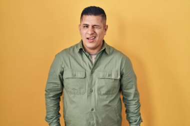 Hispanic young man standing over yellow background winking looking at the camera with sexy expression, cheerful and happy face. 