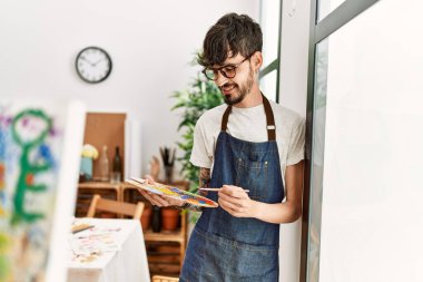 Genç İspanyol ressam mutlu bir şekilde resim stüdyosunda duruyor..