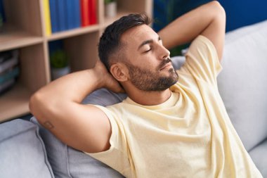 Genç İspanyol adam, ellerini başının üstüne koyup evinde kanepede oturarak rahatladı.