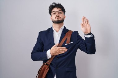 Hispanic man with beard wearing business clothes swearing with hand on chest and open palm, making a loyalty promise oath 