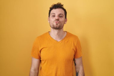 Latin asıllı genç adam sarı arka planda duruyor ve kameraya bakıyor. Canlı yayında öpücük yolluyor. Güzel ve seksi. aşk ifadesi. 