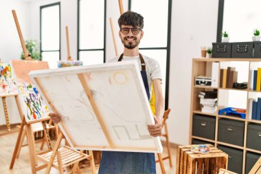 Genç İspanyol sanatçı gülümsüyor. Resim stüdyosunda tuval tutarken mutlu..